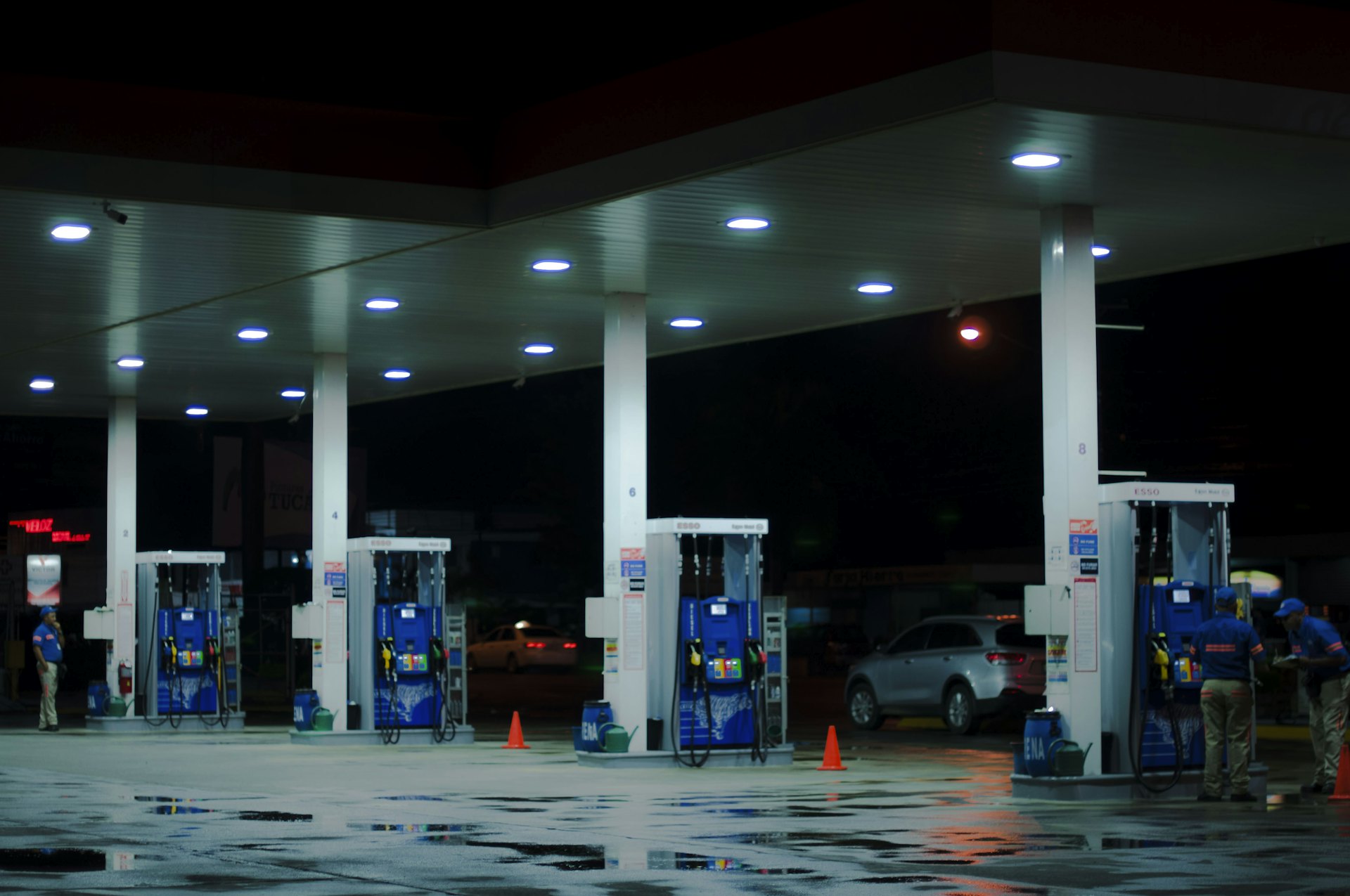 Pista de abastecimento de um posto de combustíveis iluminada à noite, com bombas e carros sob a cobertura